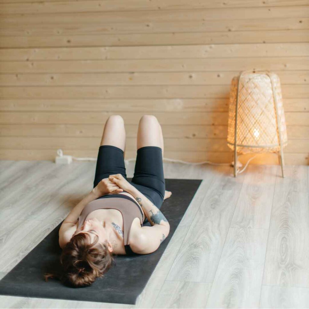kvinde ligger afslappet på en yogamåtte i et hyggeligt rum med trævægge og dæmpet belysning, fokuseret på kropsbevidsthed og indre ro.