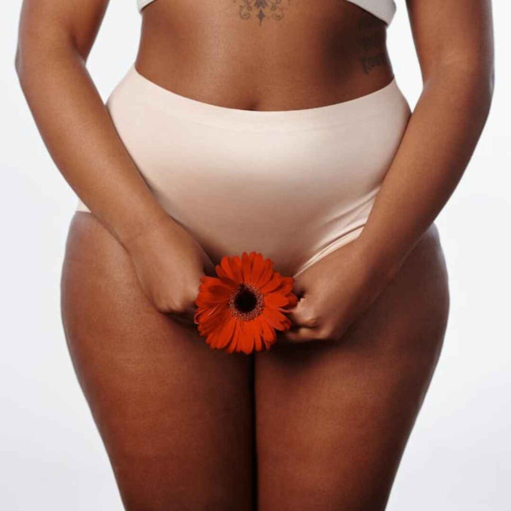 kvinde med fokus på kropsbevidsthed holder en rød blomst foran sin krop som symbol på femininitet, selvkærlighed og naturlig forbindelse.