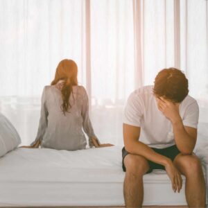 Et par sidder på sengen med ryggen til hinanden, tydeligt præget af frustration og følelsesmæssig afstand, som kan opstå ved forskellige behov hos par.