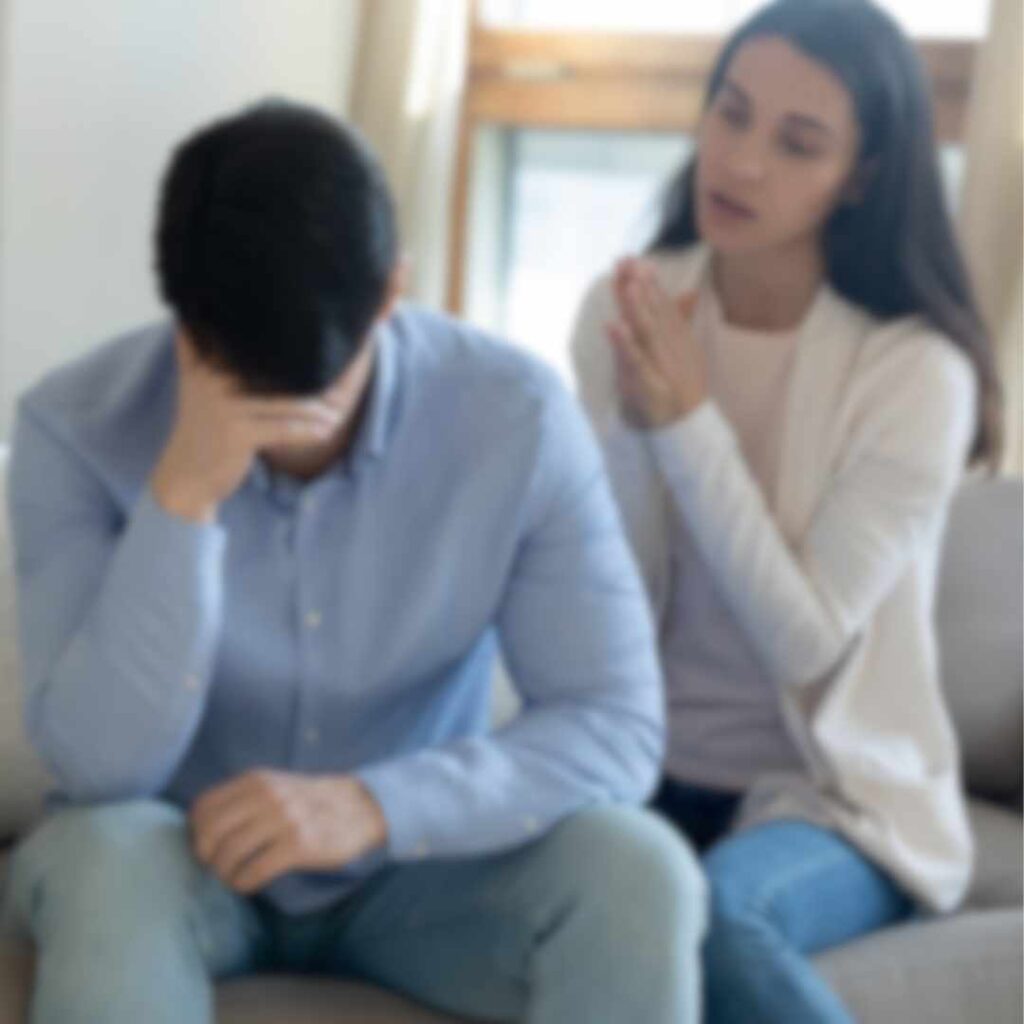 En frustreret mand sidder med hovedet i hænderne, mens en kvinde forsøger at kommunikere, hvilket afspejler vrede i parforhold og udfordringer med forståelse.