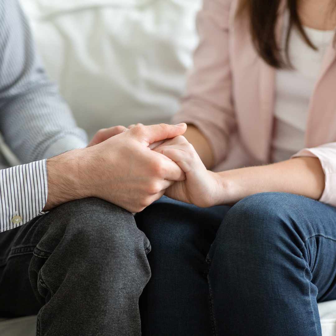 Et par sidder overfor hinanden og holder hænder, hvilket symboliserer kommunikation og forståelse i forbindelse med parterapi og forskellige behov i et forhold.