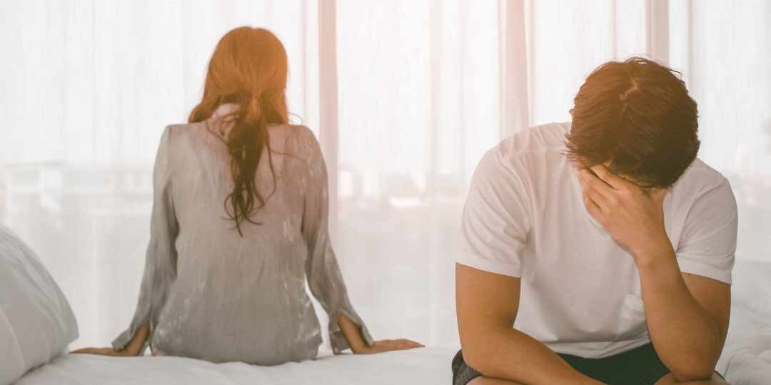 Et par sidder på sengen med ryggen til hinanden, tydeligt præget af frustration og følelsesmæssig afstand, som kan opstå ved forskellige behov hos par.